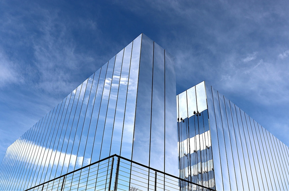 A sleek building with a glass exterior reflecting a bright blue sky and scattered clouds.
