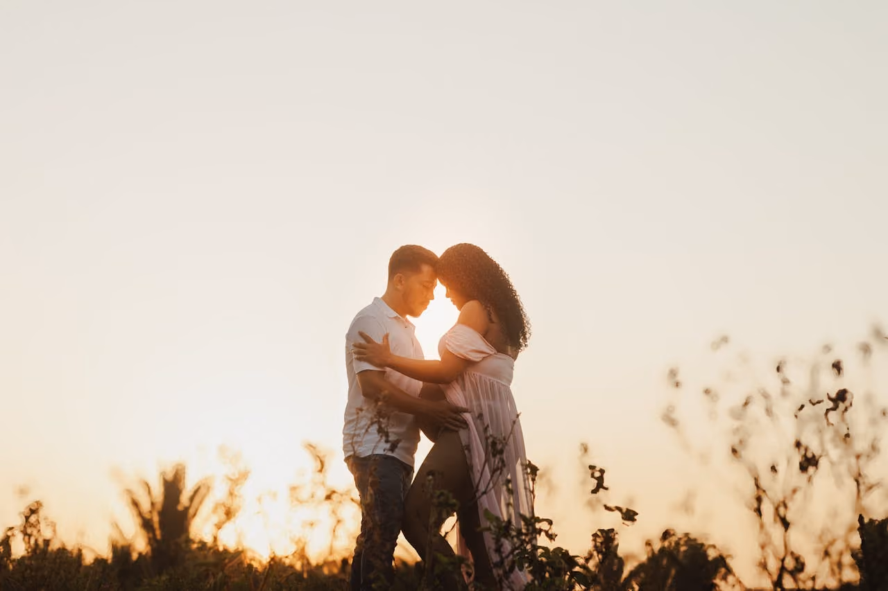 man and woman posing for maternity photoshoot framed by a beautiful sunset