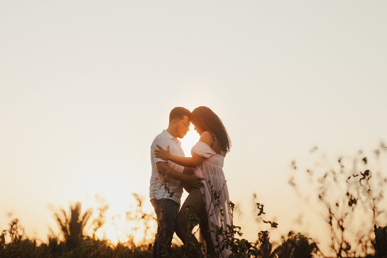 man and woman posing for maternity photoshoot framed by a beautiful sunset