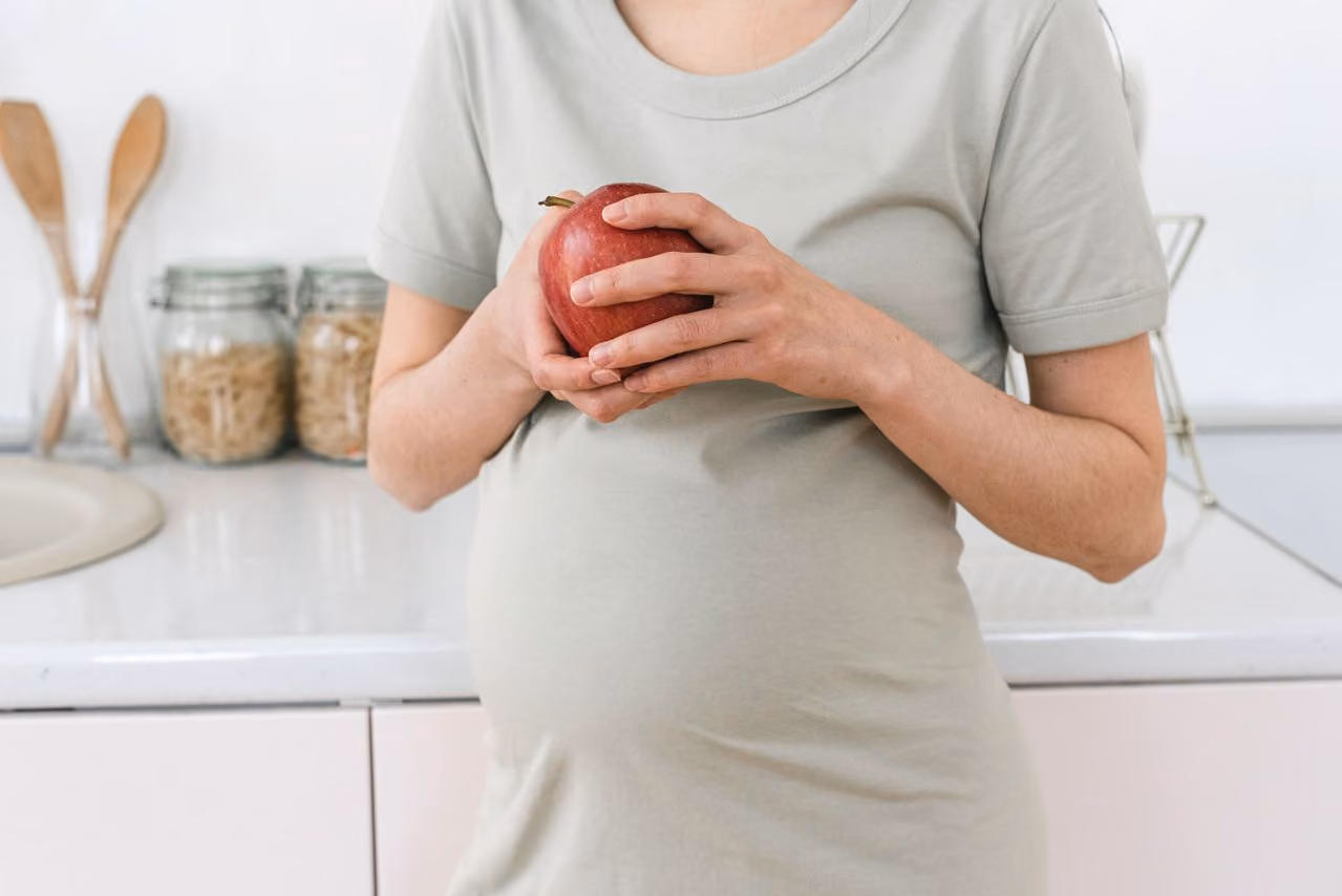 pregnant woman in a gray tshirt holding an apple