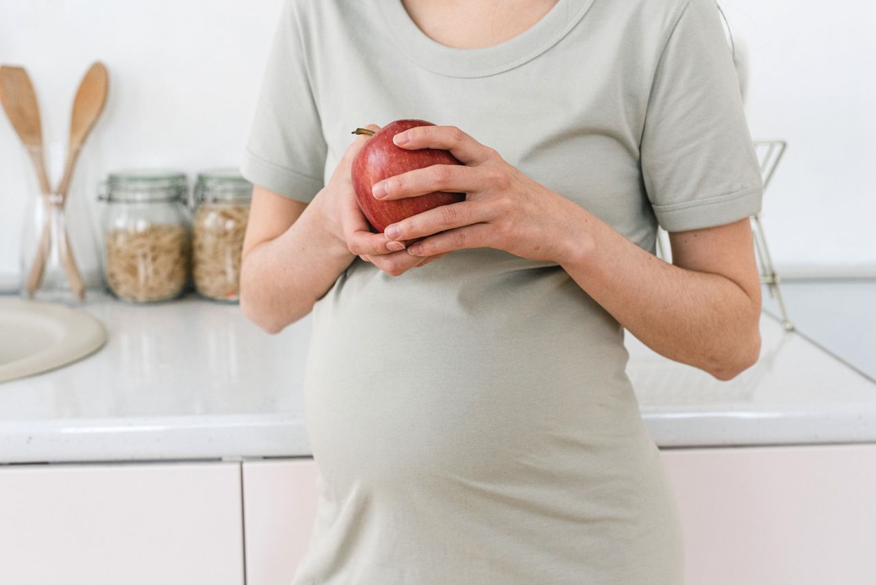 pregnant woman in a gray tshirt holding an apple