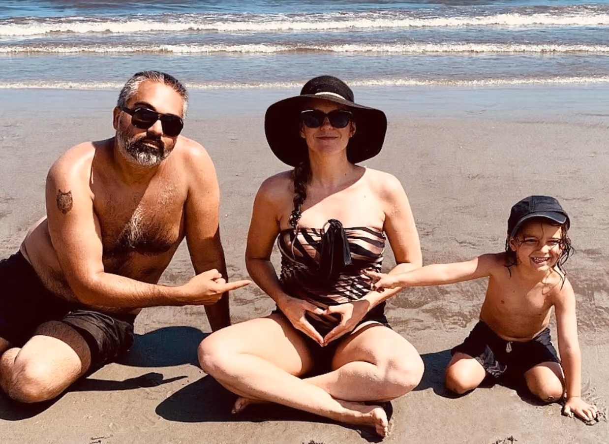 Kellee Maize with her husband and oldest child, posing in a pregnancy announcement at the beach