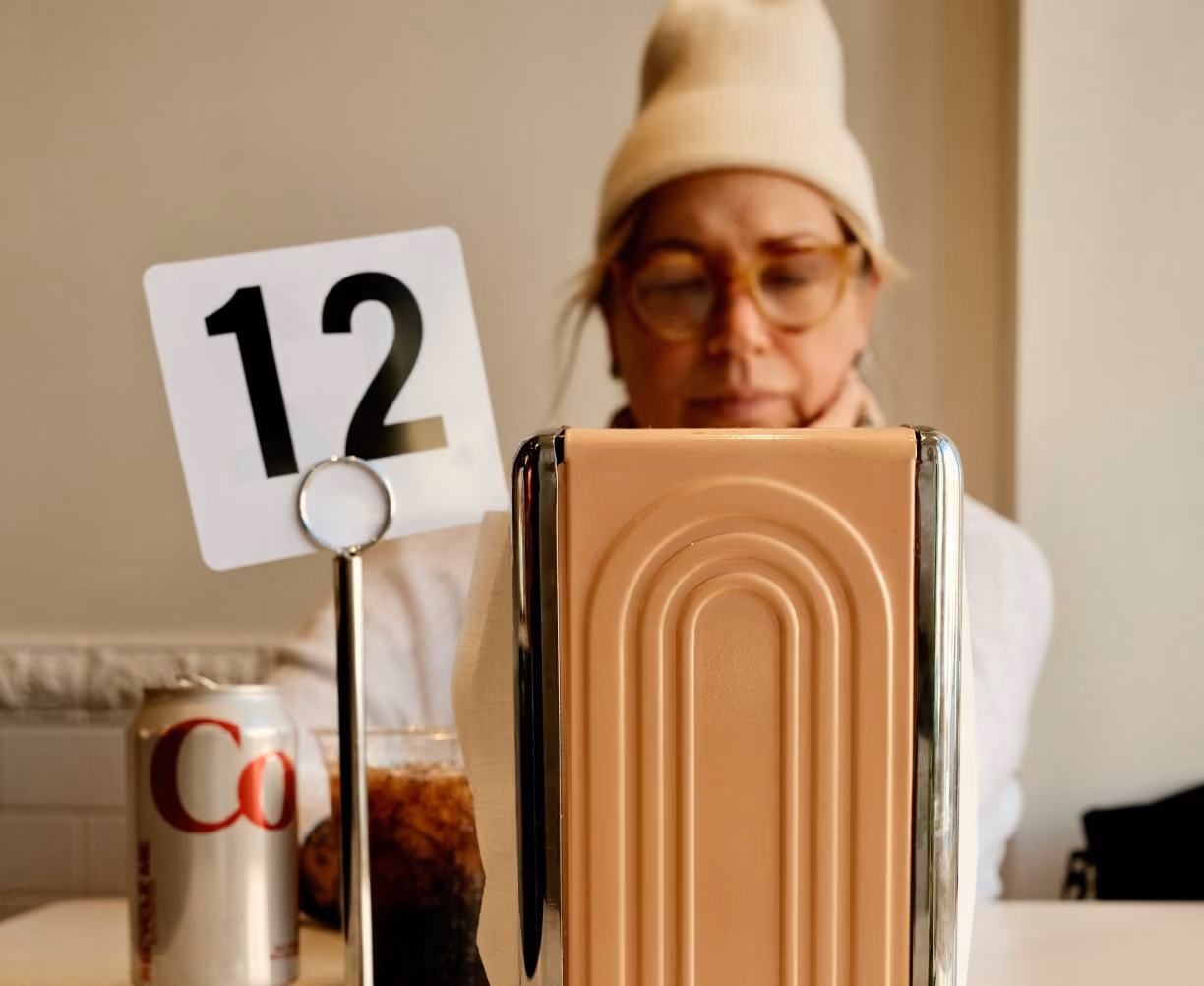 A woman sitting at a table with a can of Coke and a napkin holder.