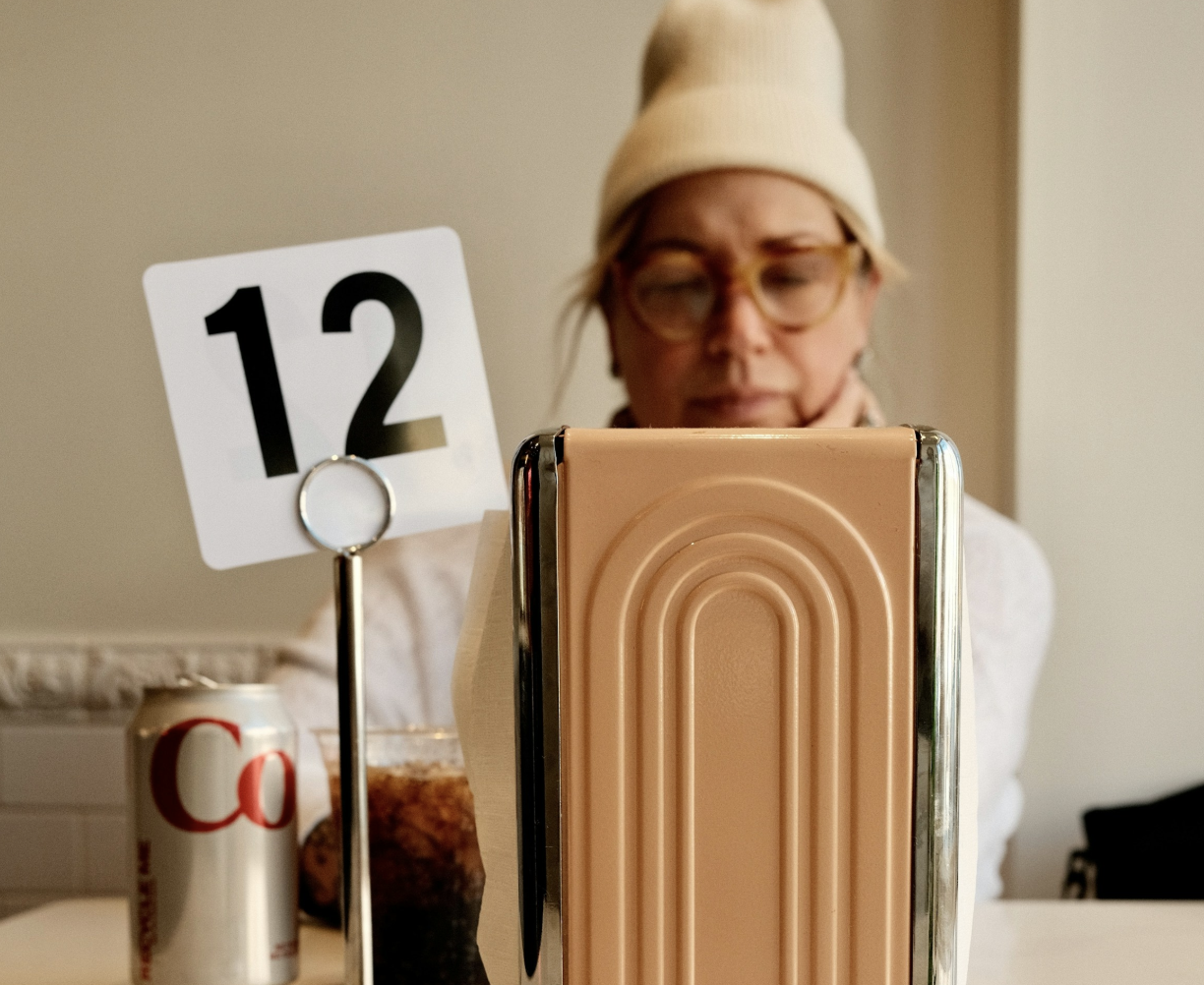 A woman sitting at a table with a can of Coke and a napkin holder.