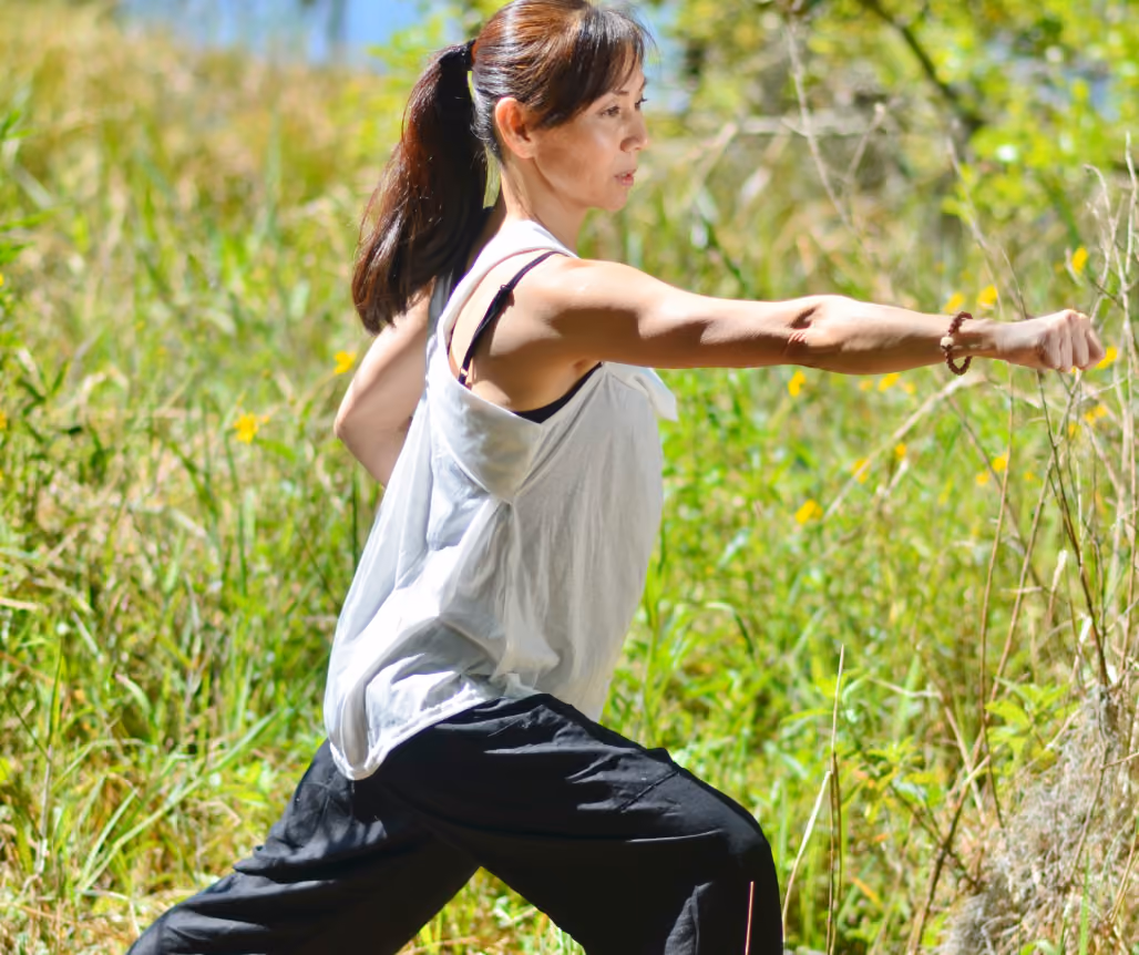 A woman in black pants and a white tank top stretching.