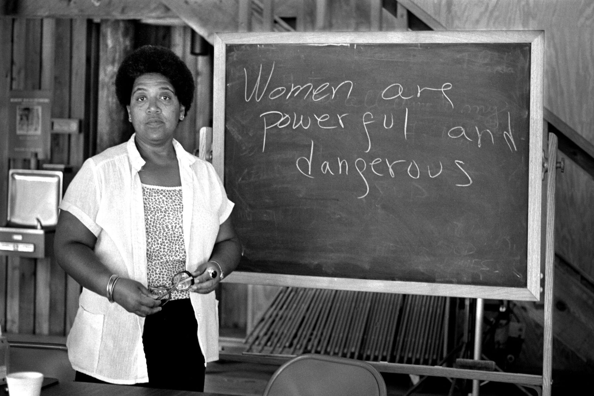 Audre Lorde standing beside a chalkboard bearing the message "Women are powerful and dangerous"