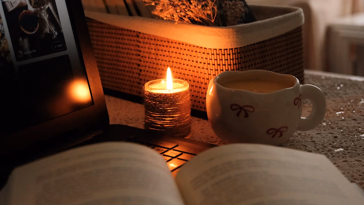 flickering candle softly illuminates the scene of an open book and warm mug of tea in a very yule-inspired scene