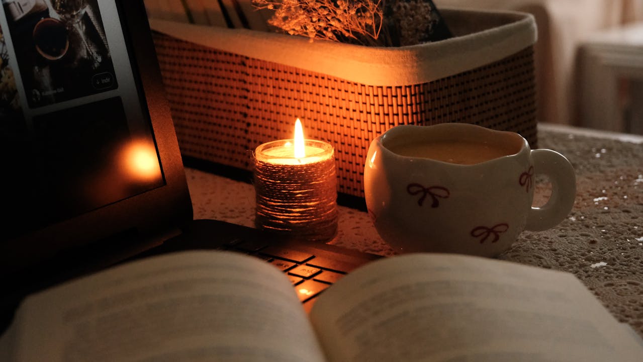 flickering candle softly illuminates the scene of an open book and warm mug of tea in a very yule-inspired scene