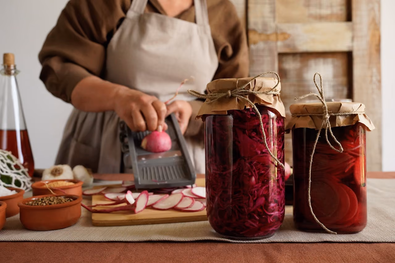 woman in a brown dress and apron slices vegetables for canning, her neatly sealed jars of preserves representing Mabon and the invitation to choose what you'll preserve from the last year and what you'll release