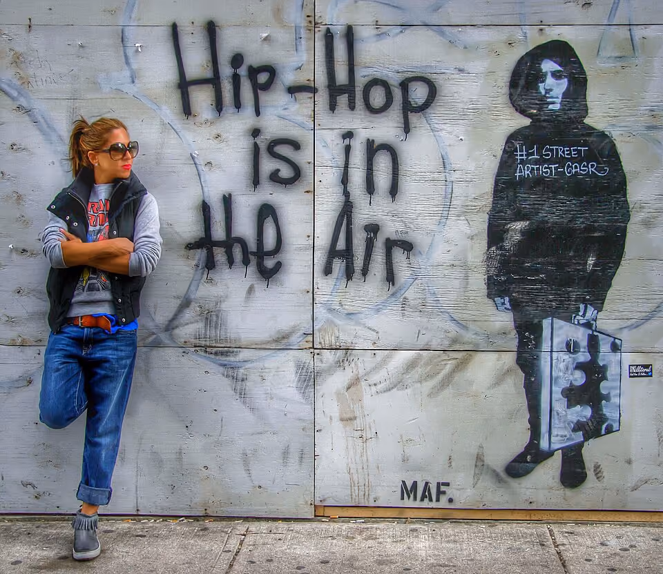 Woman in trendy clothing leans against a mural in The Bronx that reads Hi[p-Hop is in the air