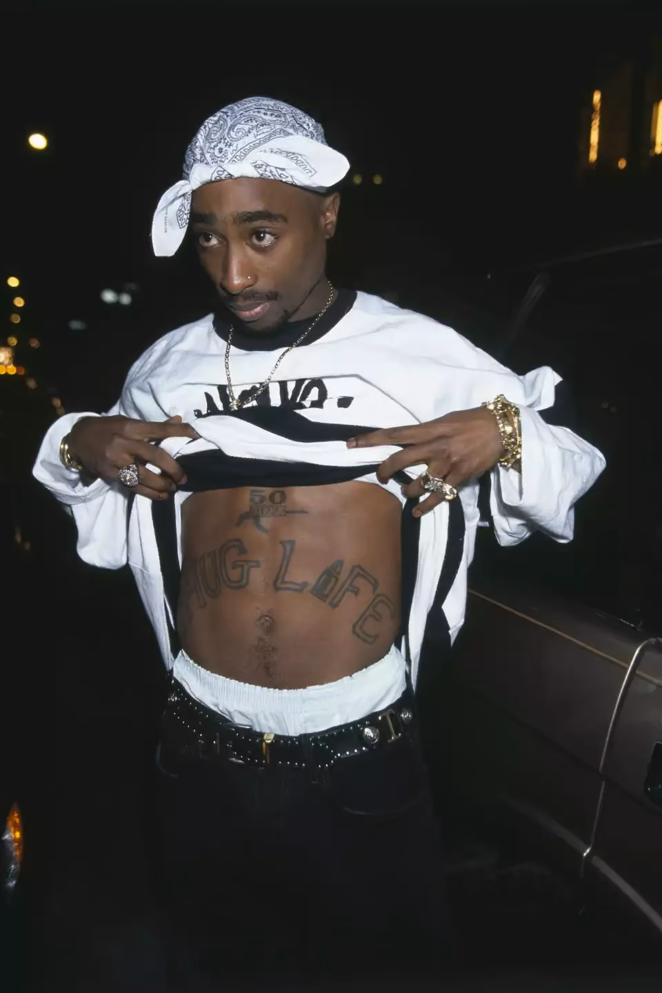 2Pac pulling up his shirt to reveal the iconic Thug Life tattoo across his stomach