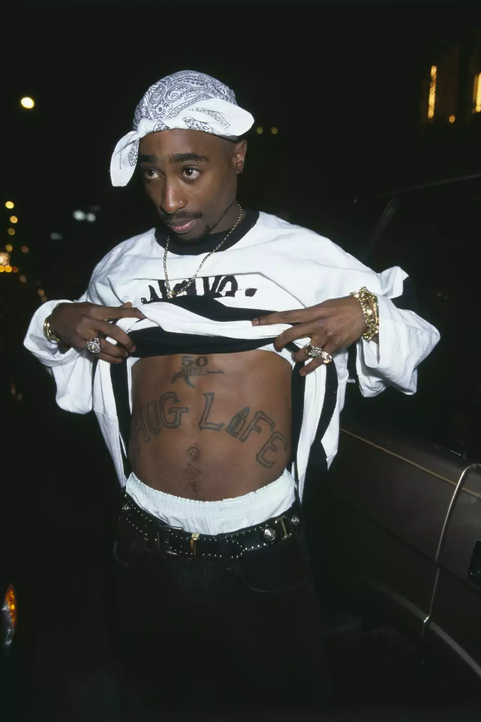 2Pac pulling up his shirt to reveal the iconic Thug Life tattoo across his stomach