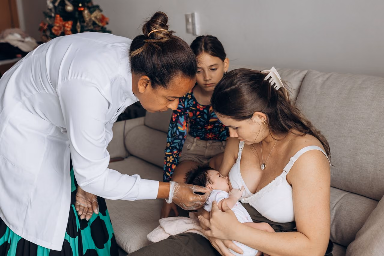 mom holding a baby while a birth doula bends toward them