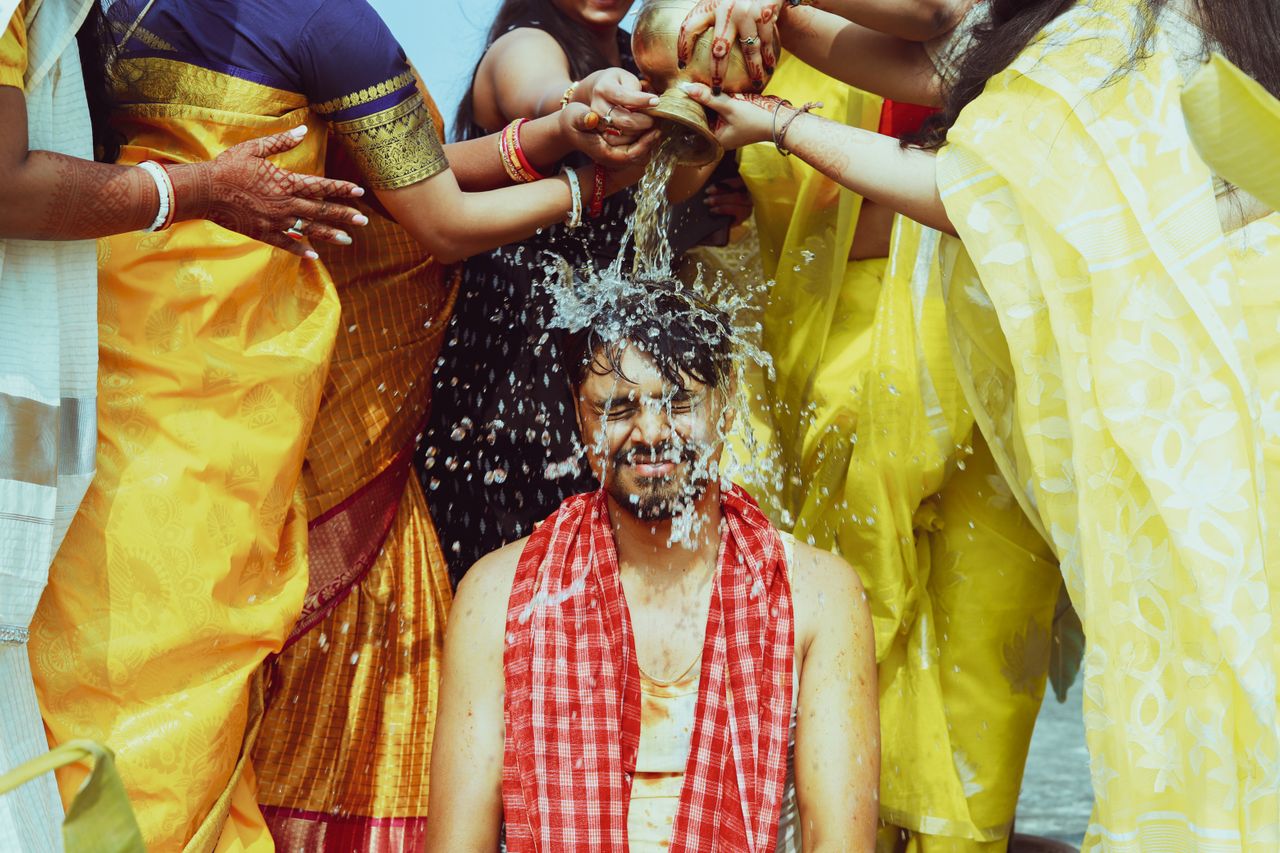 women in bright yellow sari's pour water over the head of a seated man as a part of a spiritual ritual