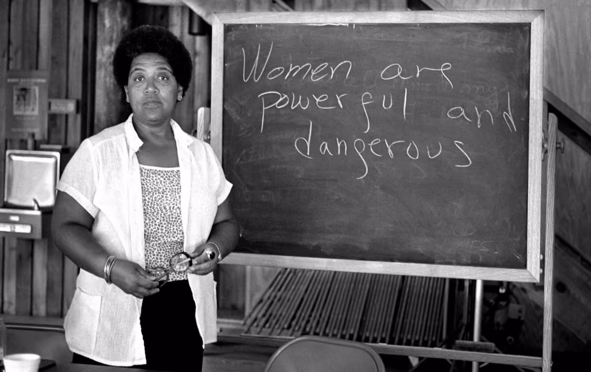 Audre Lorde standing beside a chalkboard bearing the message "Women are powerful and dangerous"