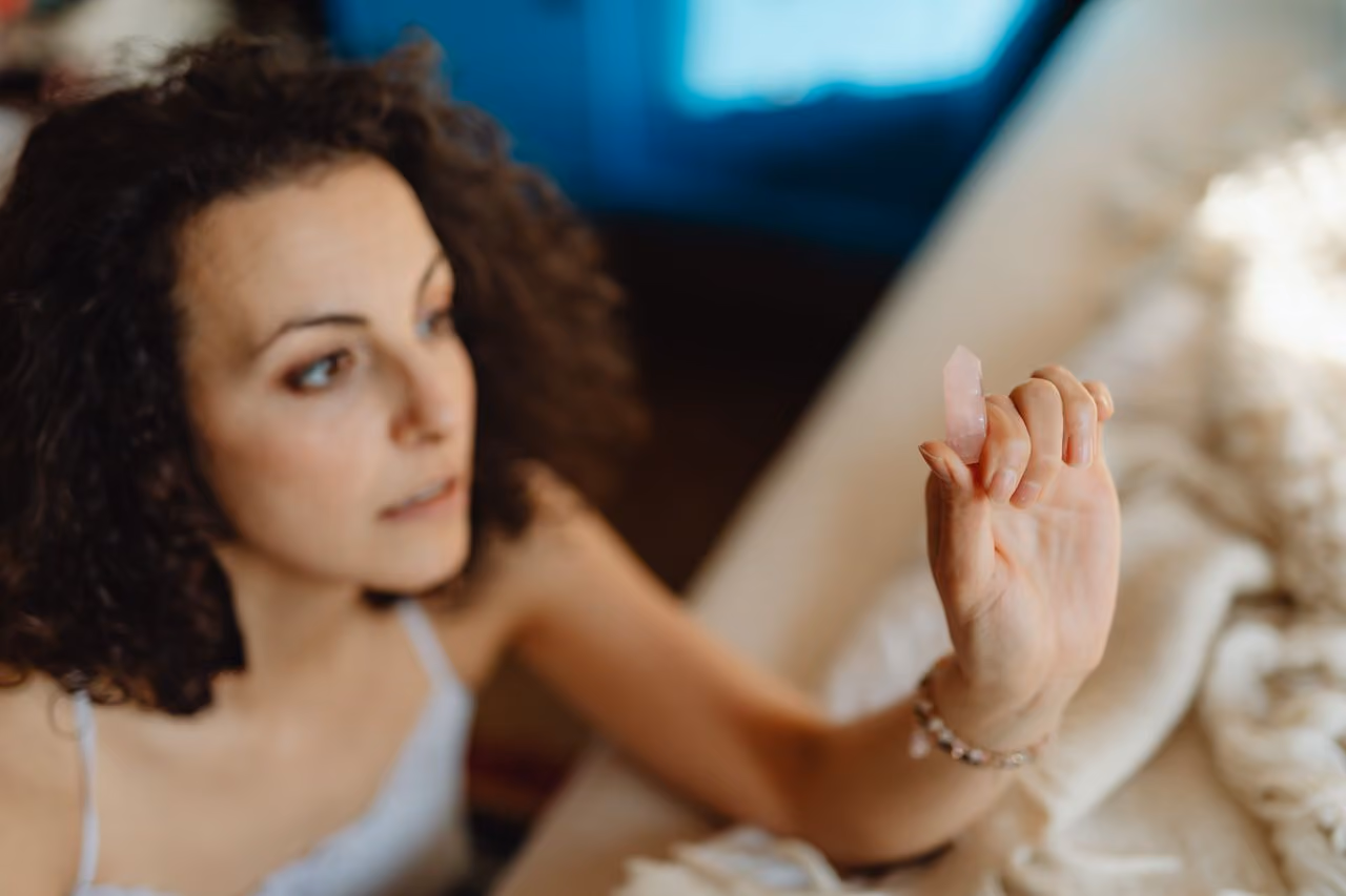 woman holding up a piece of rose quartz, contemplating the meaning of the stone for her spiritual practice