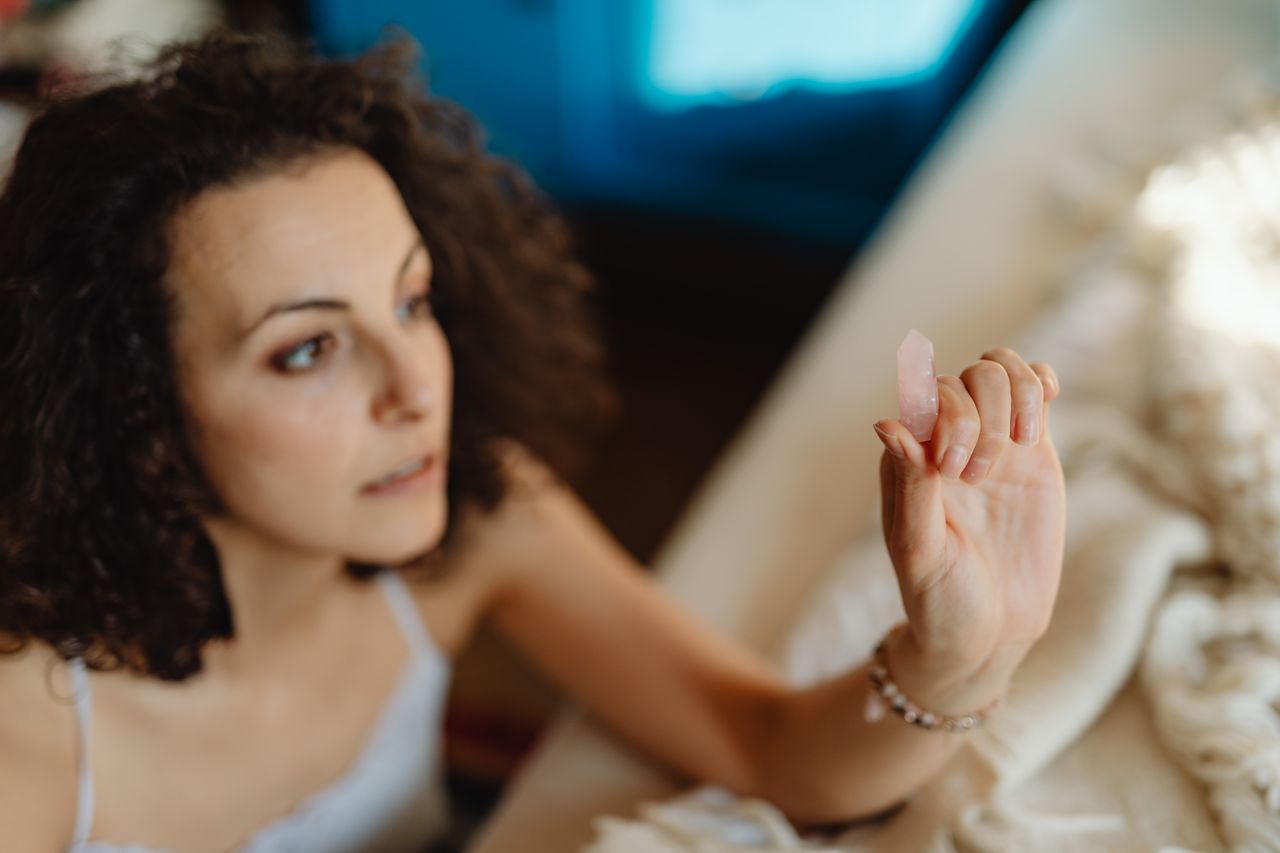 woman holding up a piece of rose quartz, contemplating the meaning of the stone for her spiritual practice