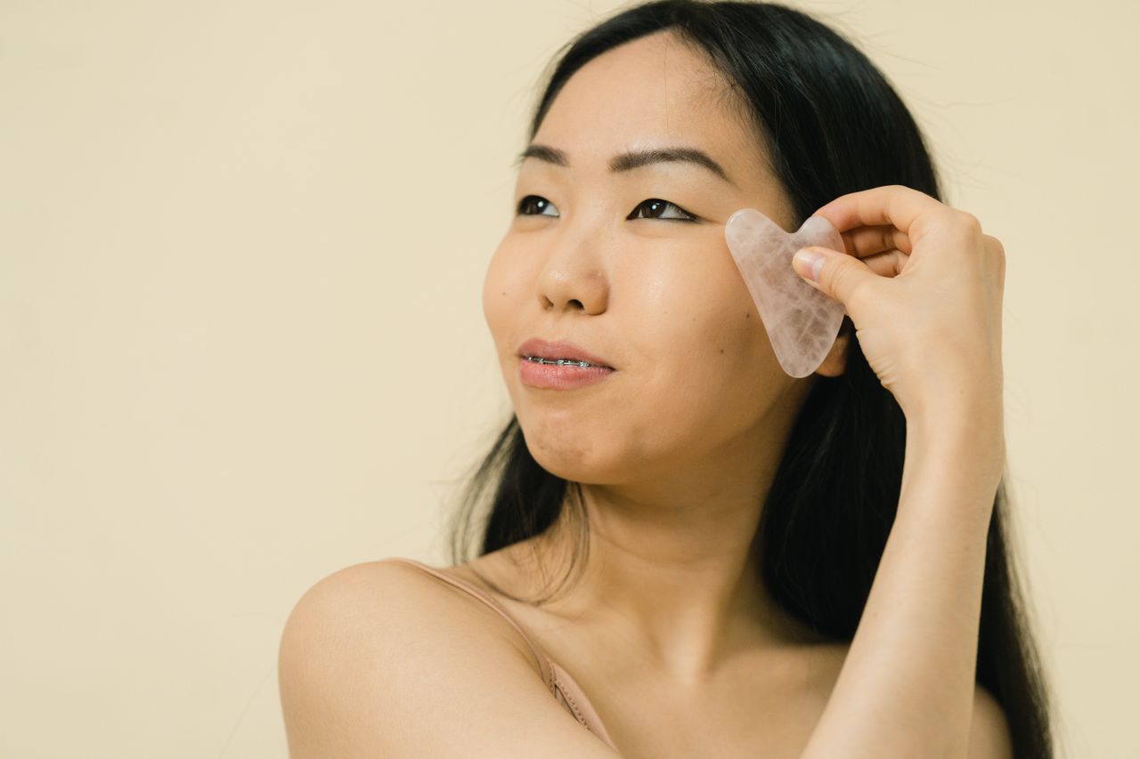 woman running a rose quartz gua sha over her cheek