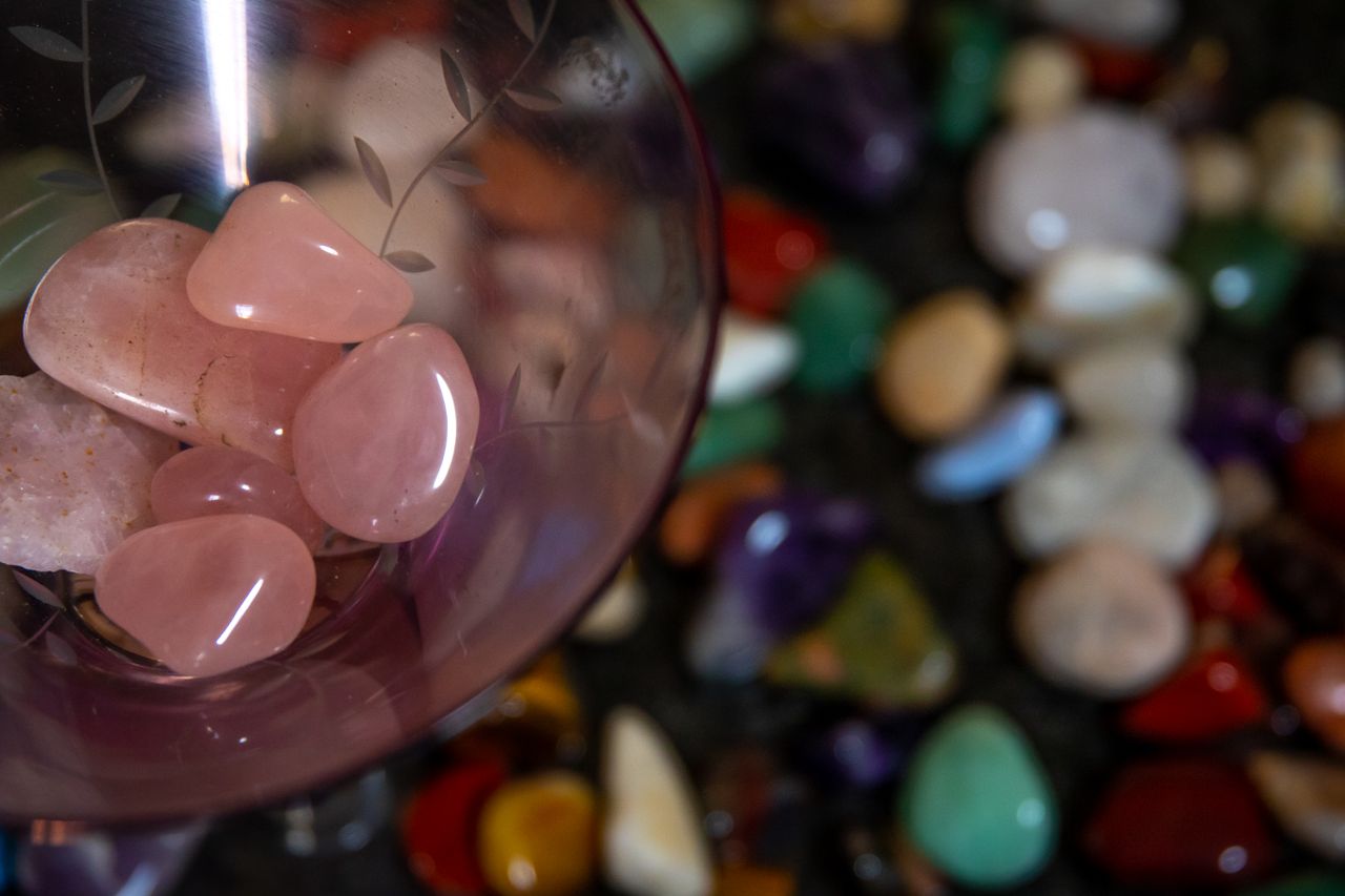 bowl of polished rose quartz stones in focus, with an array of other crystals and stones out of focus in the background