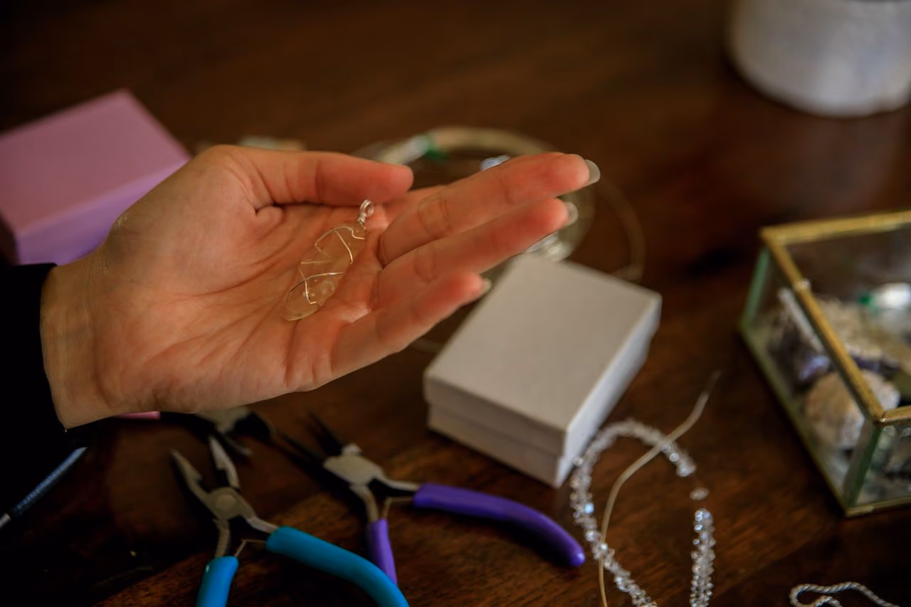 woman holding a citrine pendant in her open palm with jewelry-making tools strewn about the table nearby