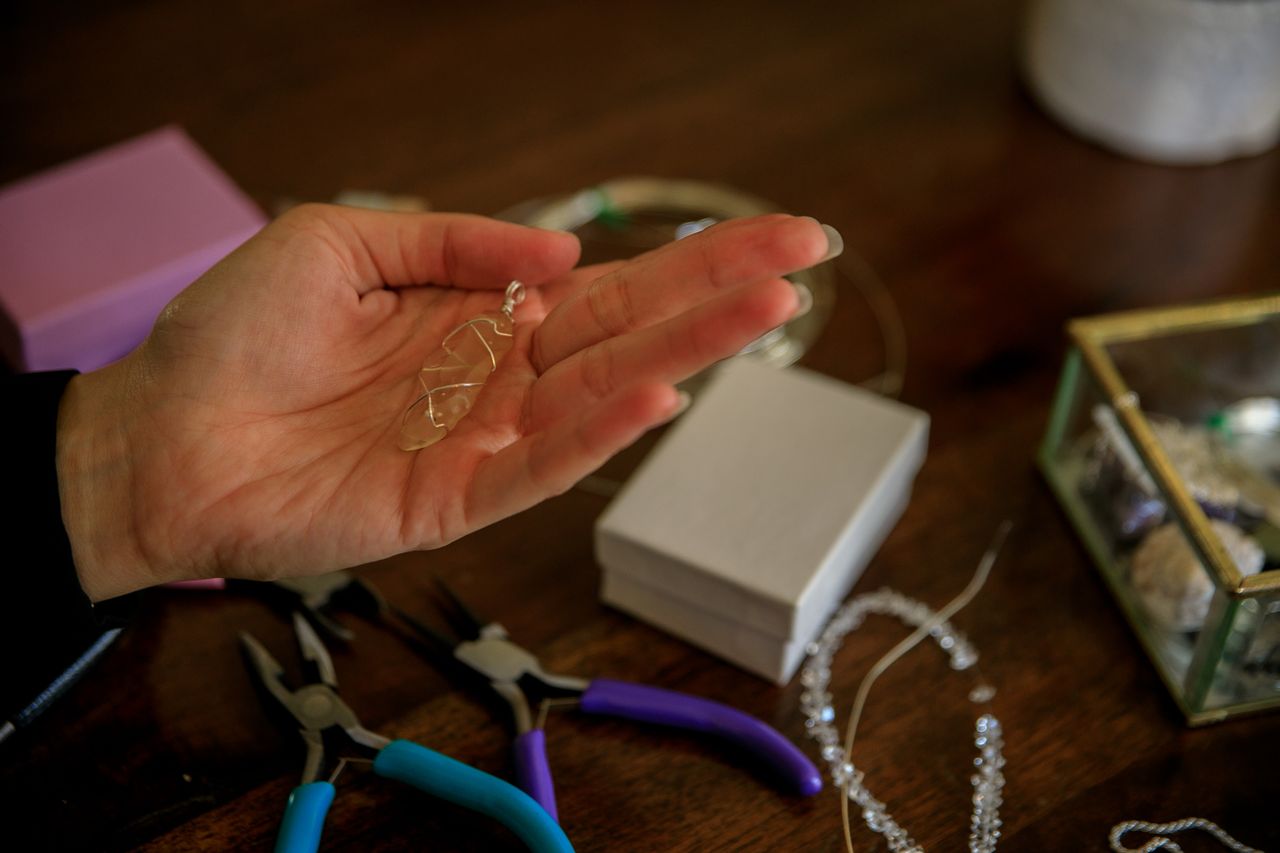 woman holding a citrine pendant in her open palm with jewelry-making tools strewn about the table nearby