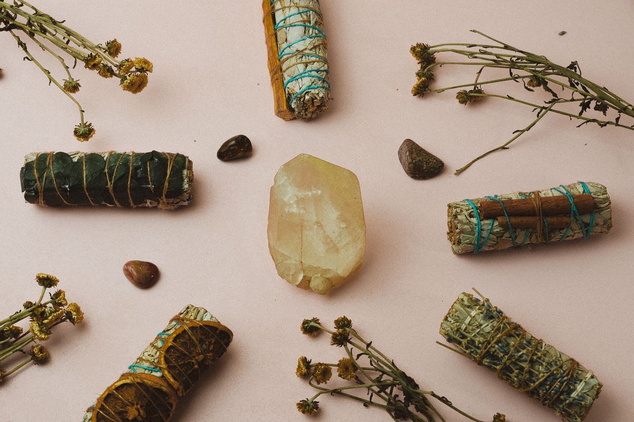 a soft yellow citrine stone surrounded by other crystals and a few bundled herb smudge sticks associated with spiritual cleansing