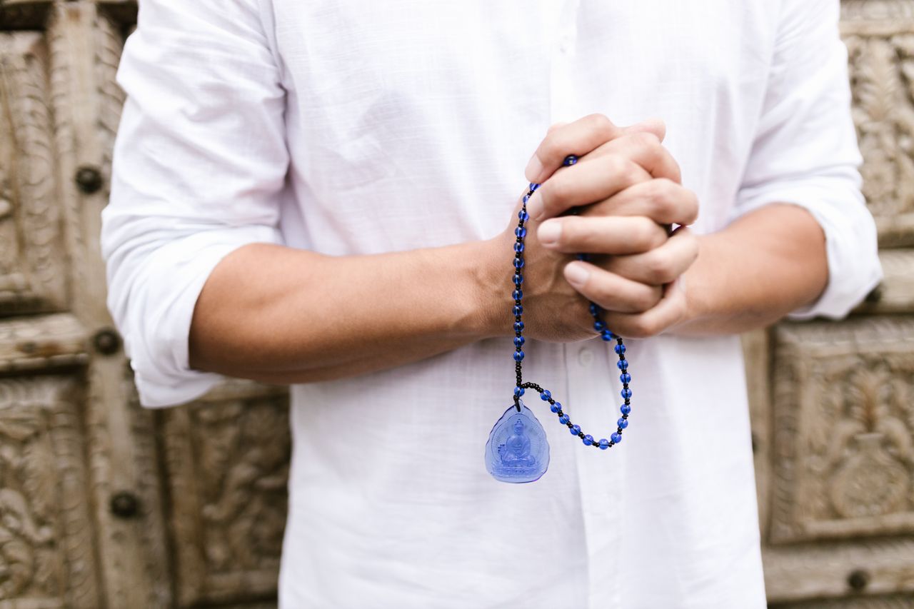 man in a loose white shirt holding lapis lazuli prayer beads in his clasped hands as he meditates