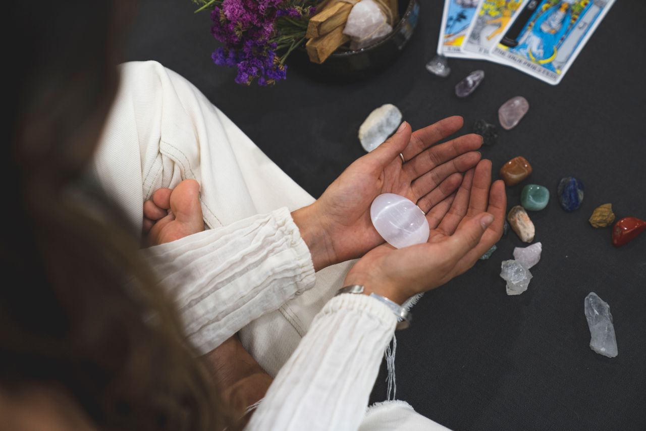 woman seated with crystals and tarot cards in front of her, holding a moonstone egg in her cupped hands