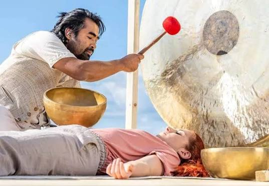 man using a gong and Tibetan bowl in a sound bath