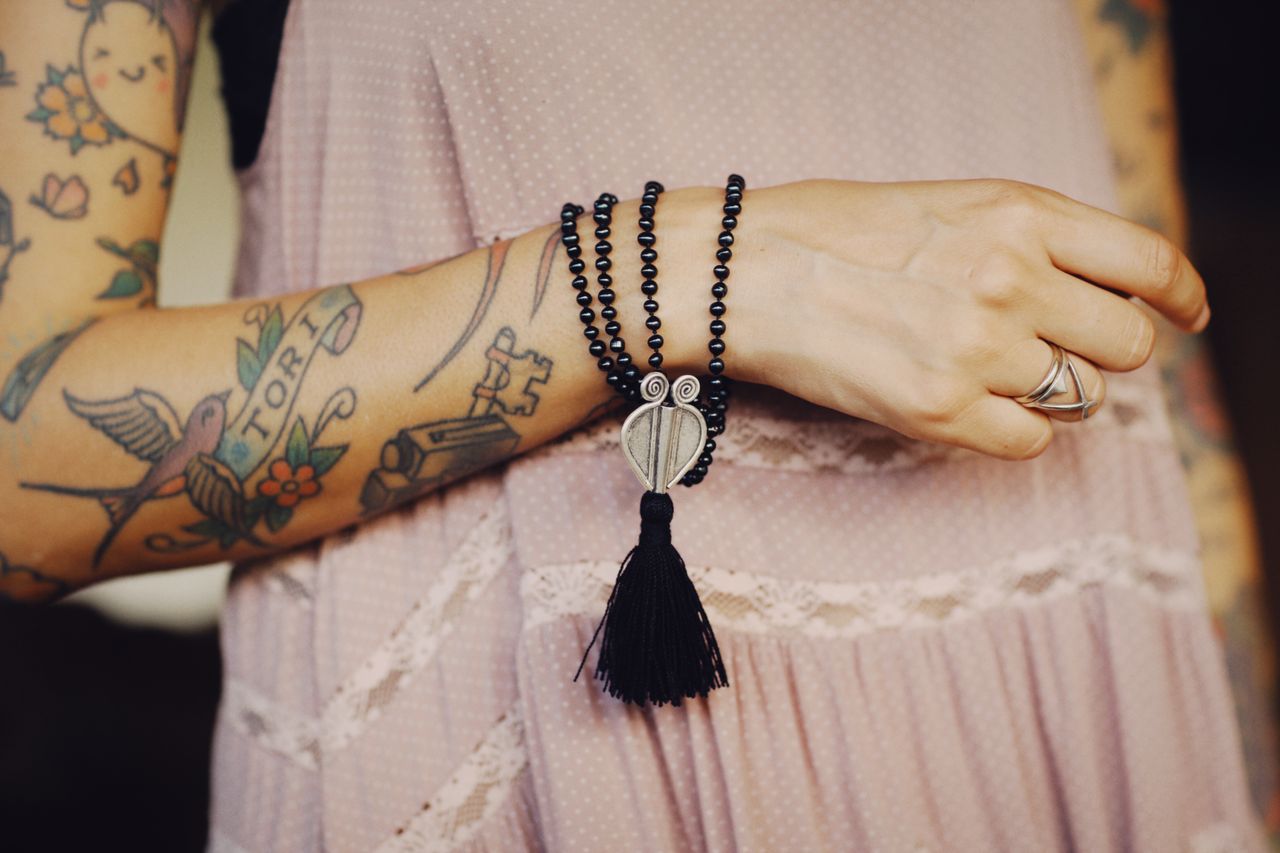 spiritual woman with tattooed arms and shiny black tourmaline prayer beads draped over her wrist