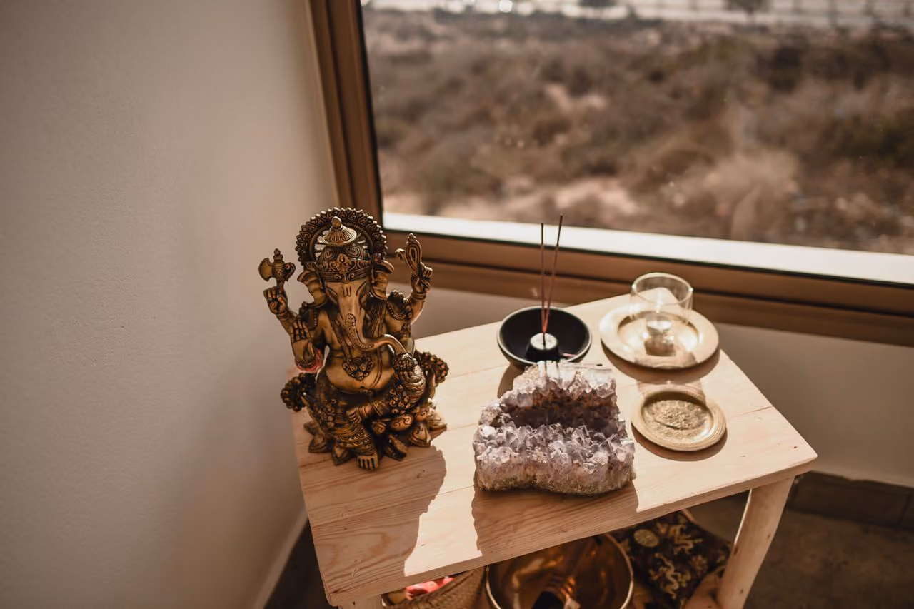 a small home altar set up with a statue, incense, and chunk of geode amethyst