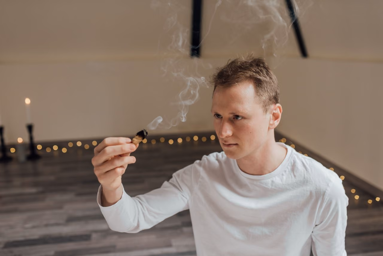 man wafting smoke from a burning smudge stick around himself for personal energy cleansing