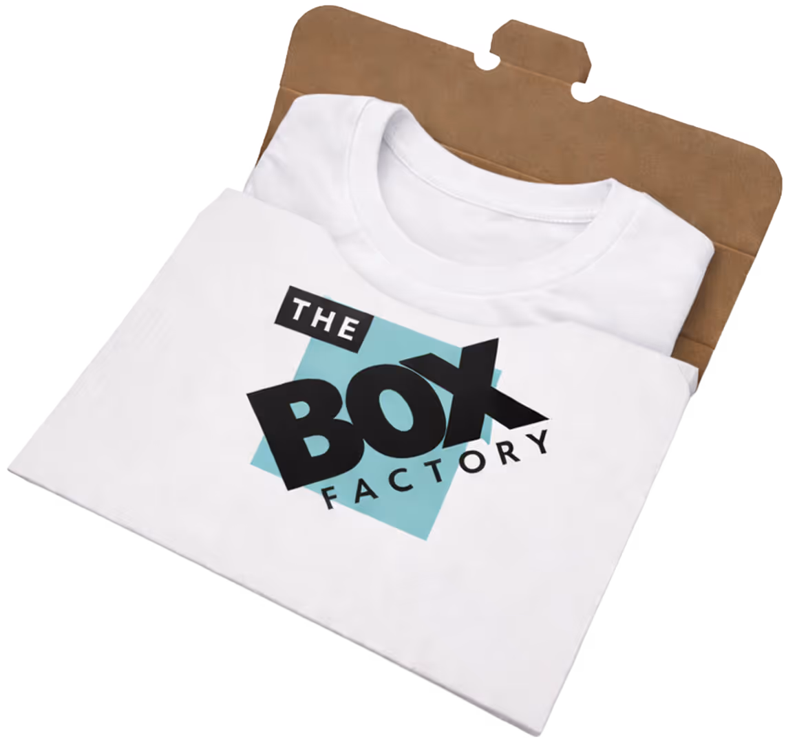 White folded T-shirt with 'The Box Factory' logo in black and light blue printed on the front, partially inside a brown cardboard packaging.