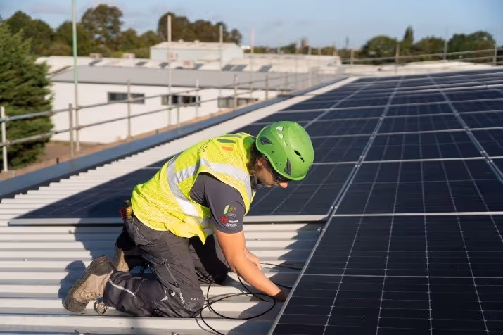 Worker wearing a green helmet and yellow safety vest installing solar panels on our rooftops.