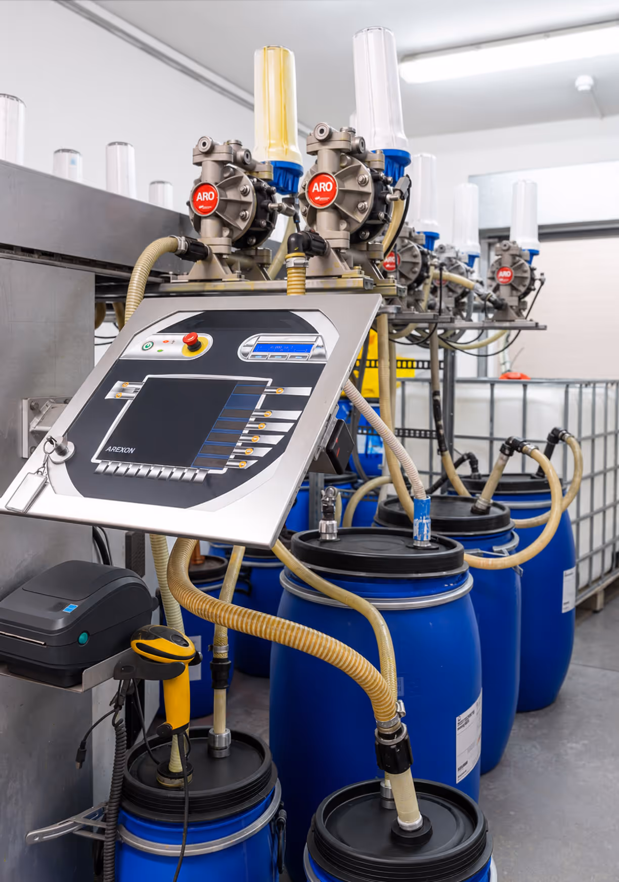 Industrial color mixing machine with control panel and blue barrels connected by yellow tubes.