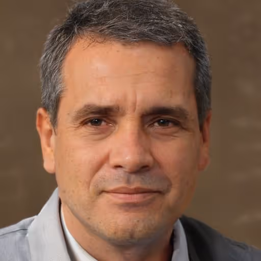 Portrait of a middle-aged man with short gray hair wearing a light gray shirt against a brown background.
