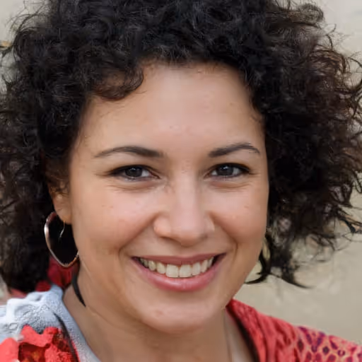 Smiling woman with curly dark hair wearing hoop earrings and a red patterned top.