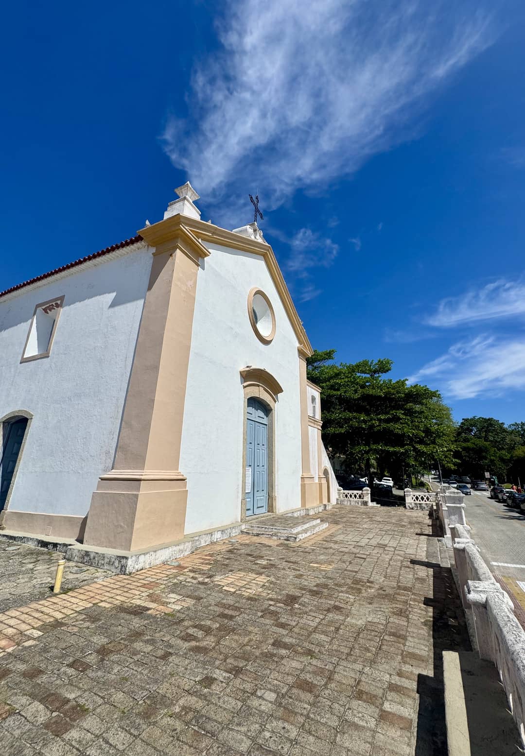 A small pastel-blue and beige historic church with a cross on top, photographed from a low angle under a deep blue sky with wispy clouds.