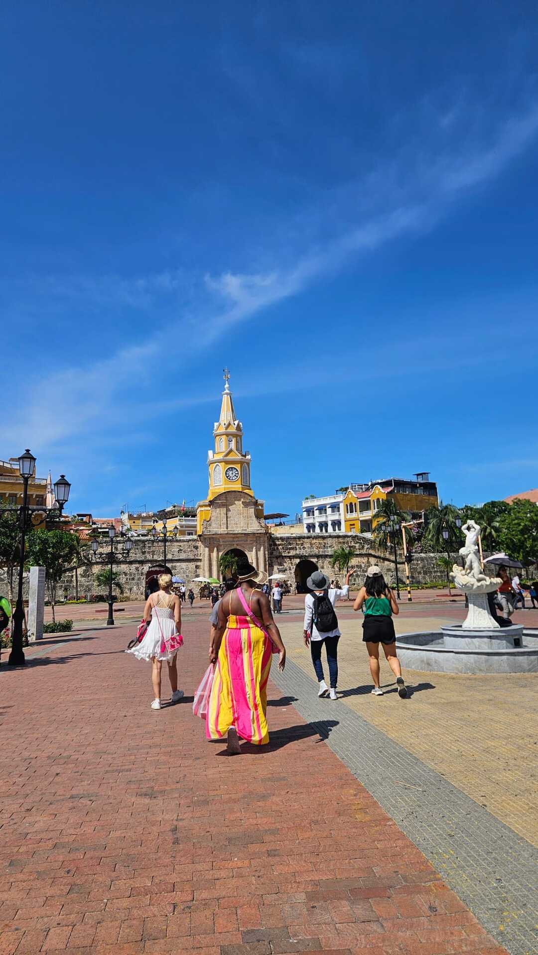 Travelers walking through Cartagena’s Old Town plaza with the iconic clock tower in the background.