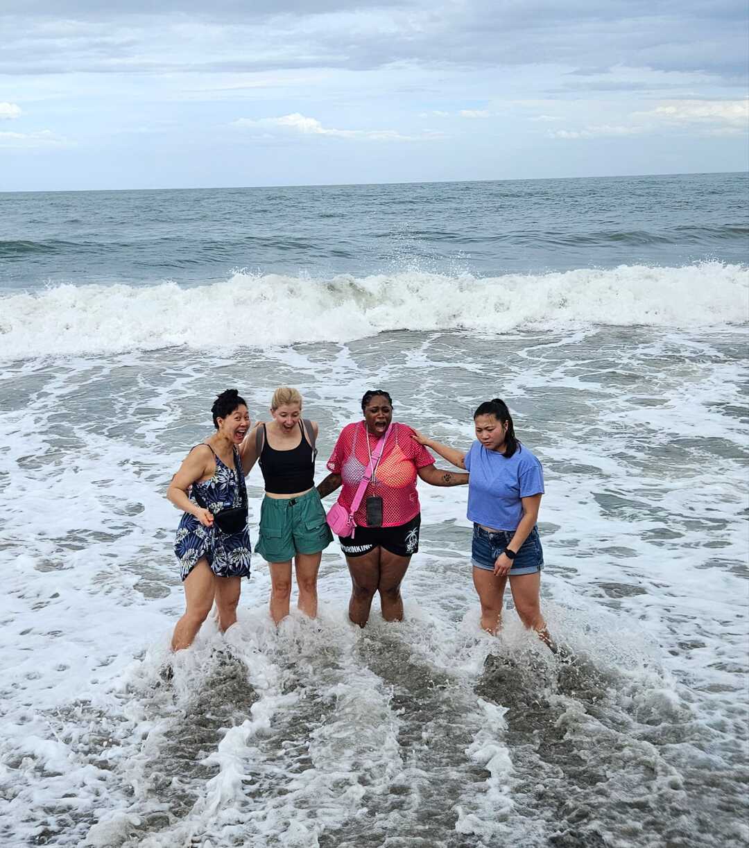 Friends holding hands and laughing while walking into ocean waves at a Colombian beach.
