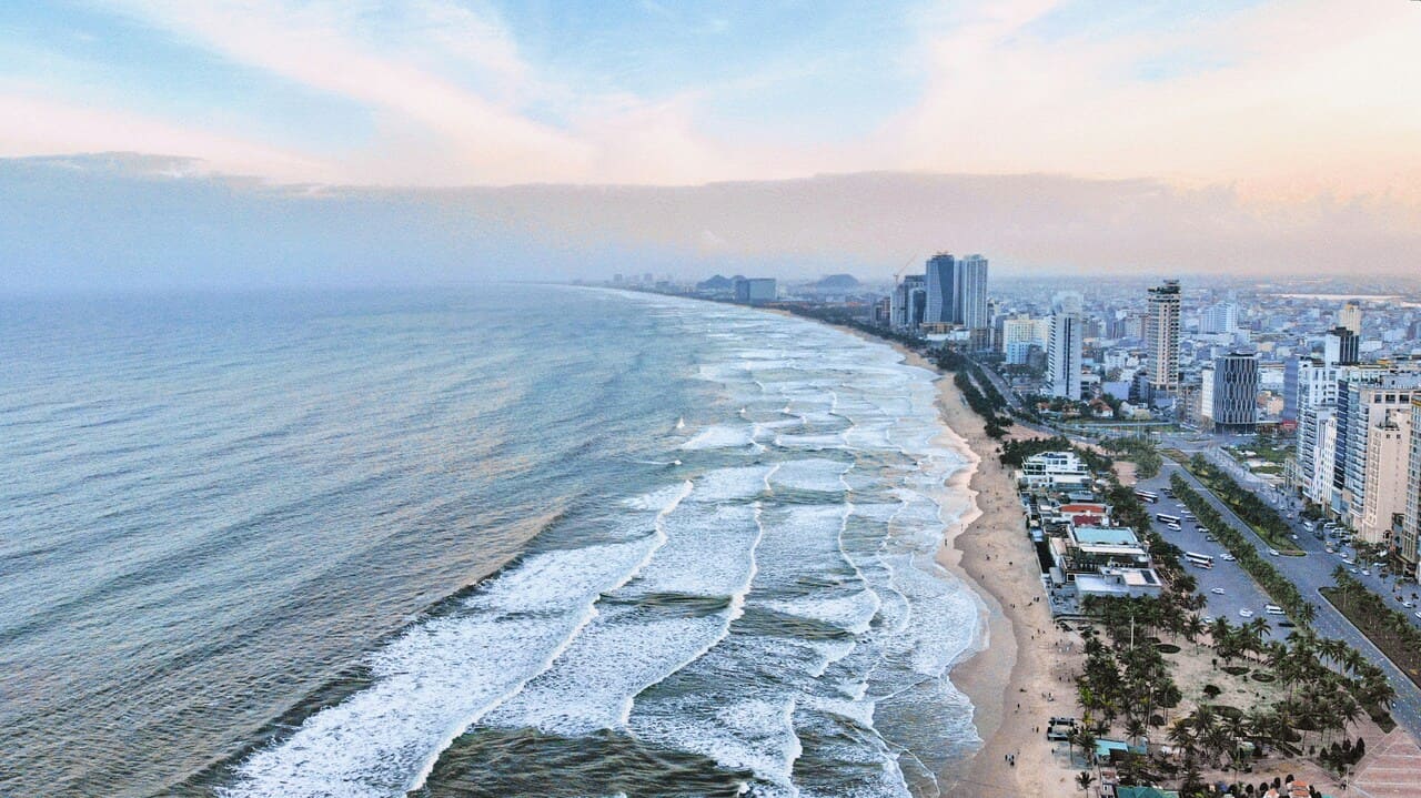 Aerial view of My Khe Beach and Da Nang skyline along Vietnam's central coast with waves rolling onto the sandy shoreline.