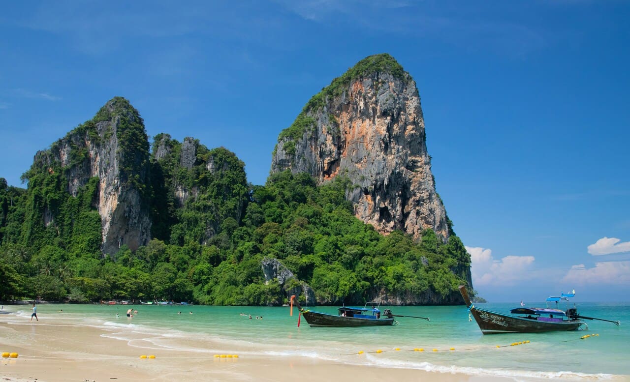 Railay Beach in Krabi Thailand with longtail boats, turquoise water, and limestone cliffs