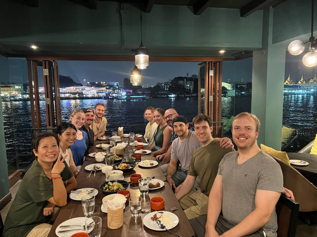 Group of Under30Experiences travelers having dinner at a riverside restaurant in Bangkok, Thailand