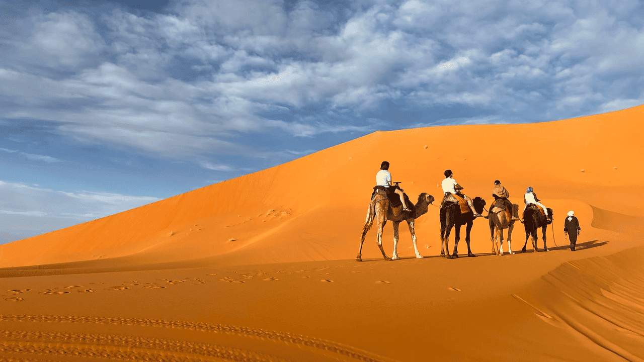 Travelers riding camels across the Sahara Desert sand dunes