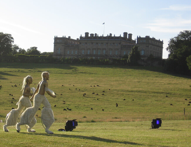 Gold painted satyr's on bouncy stilts running across a Meadow.