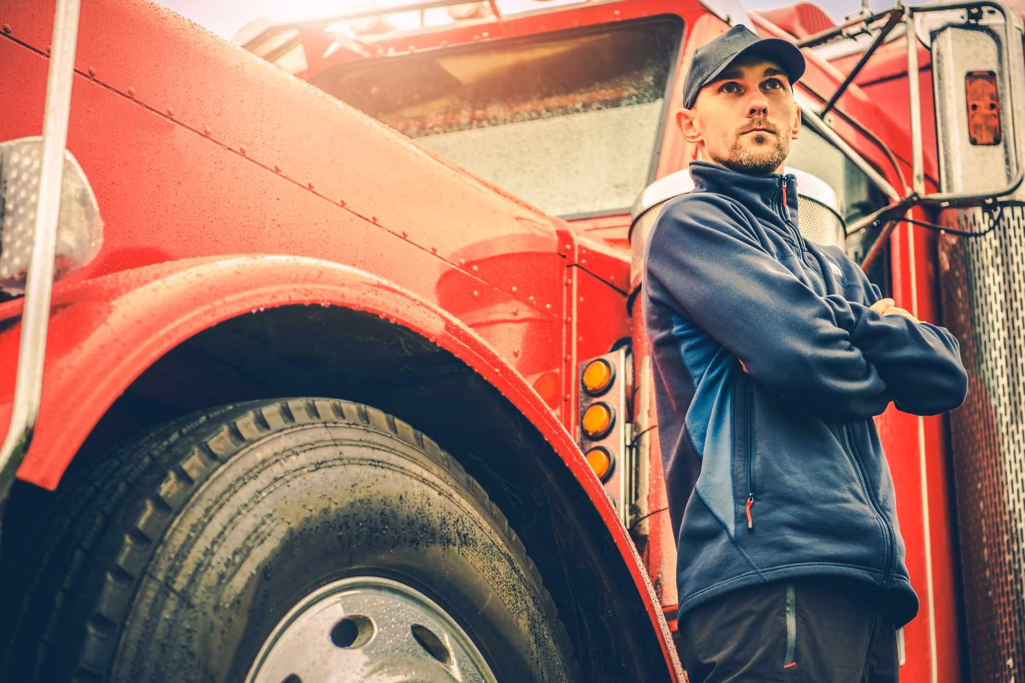 A truck driver stands beside his red semi truck