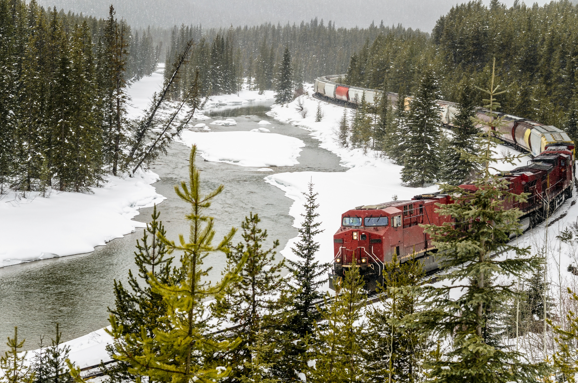 A freight train moves along a snowy track in a scenic setting