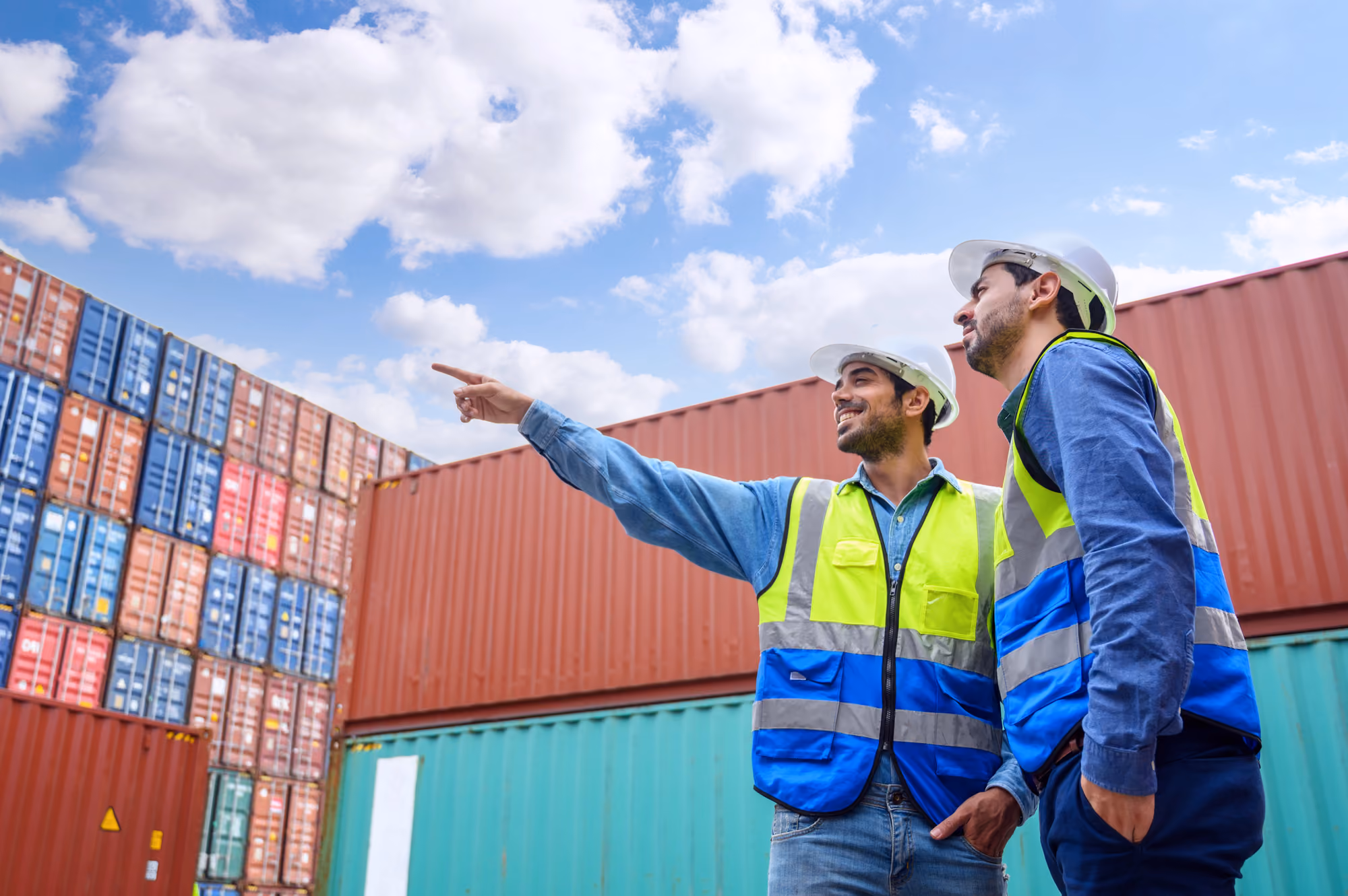 Two logistics workers stand alongside containers at a port