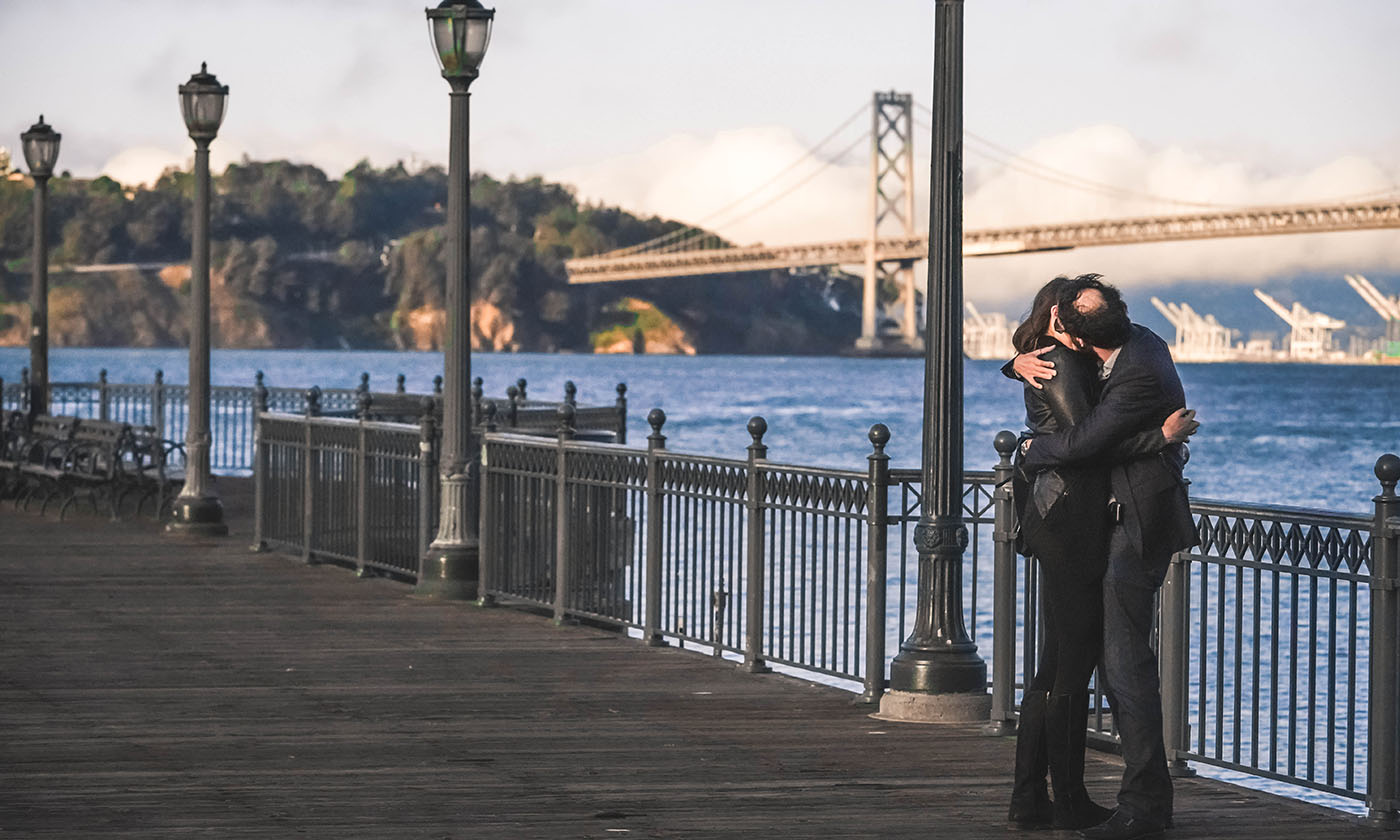 Couple embracing on a San Francisco pier with the Bay Bridge in the background