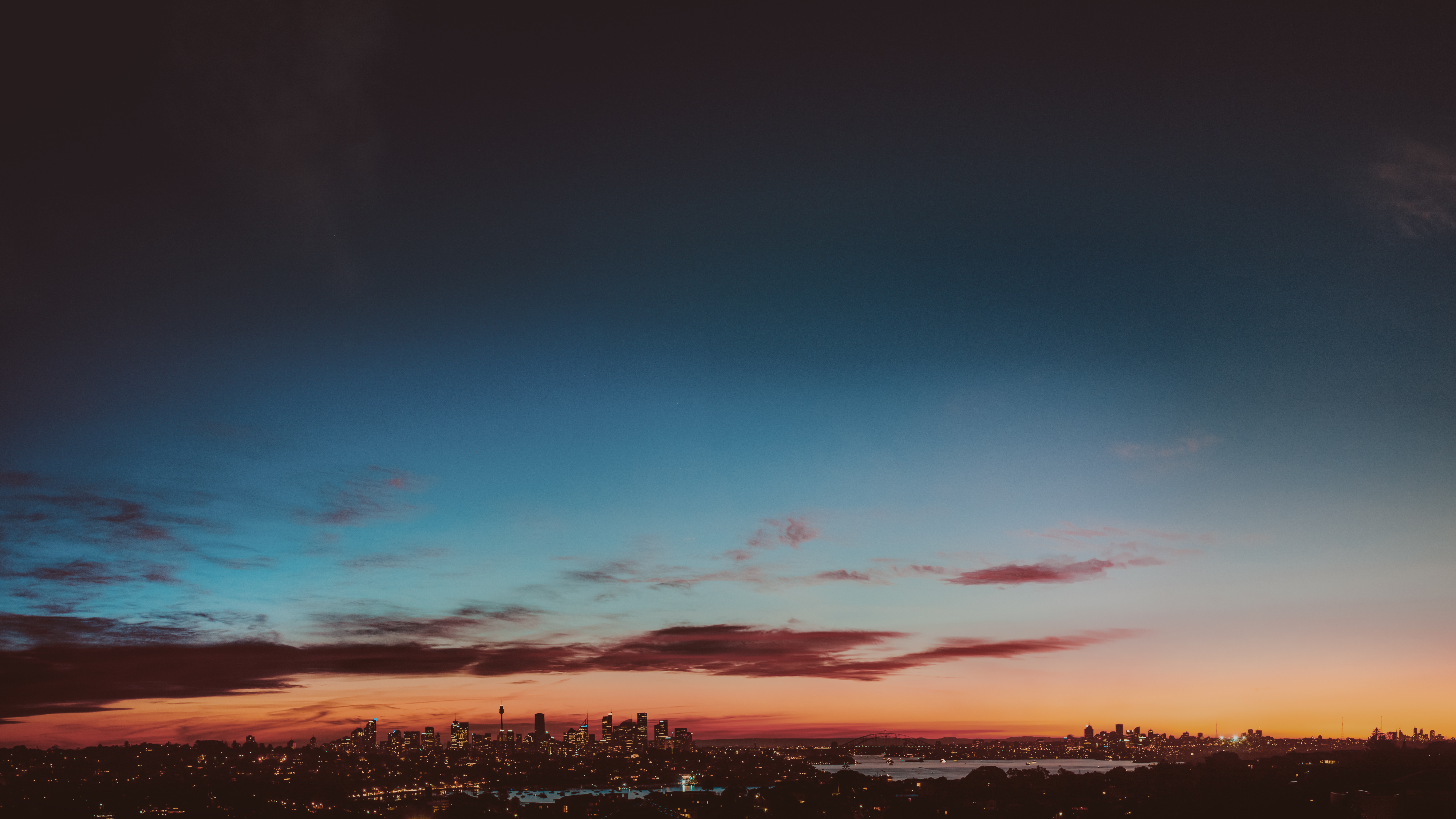 Aerial silhouette of the Sydney skyline at twilight with deep blue sky transitioning to orange on the horizon
